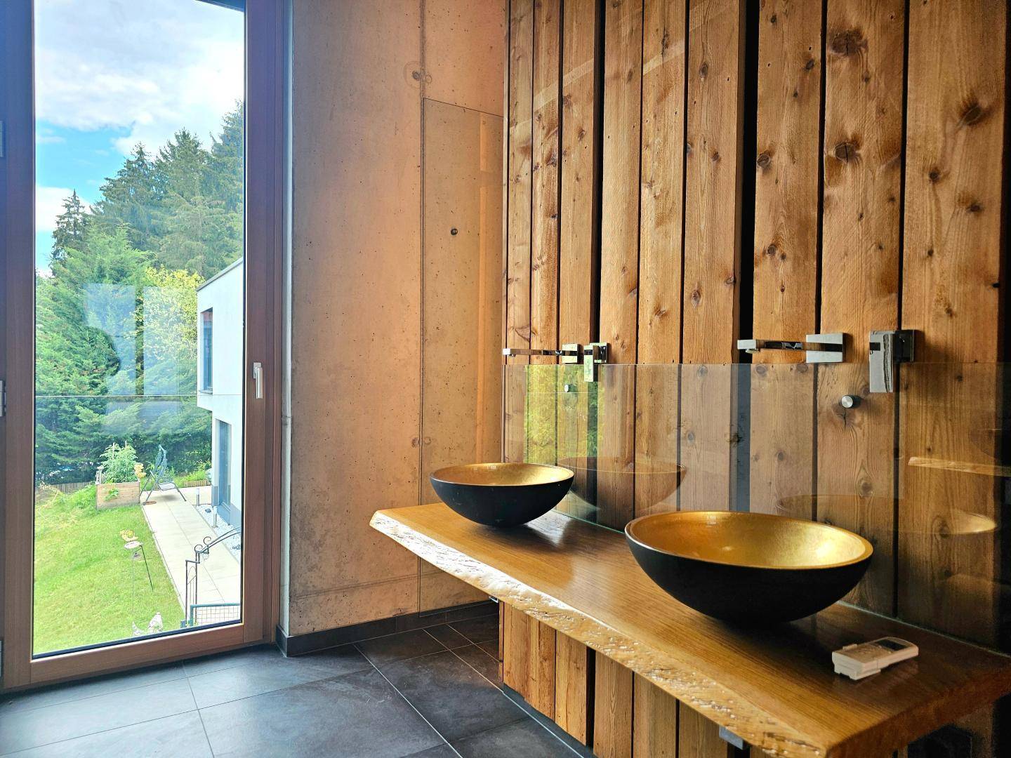 Detailansicht der modernen Waschbecken mit goldenen Schalen und großem Fenster mit Waldblick.