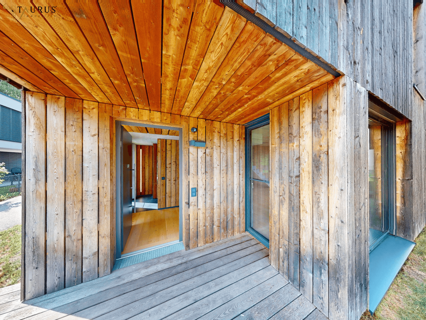 Eingangsbereich mit Holzverkleidung und kleiner Terrasse, die zum Haus führt.