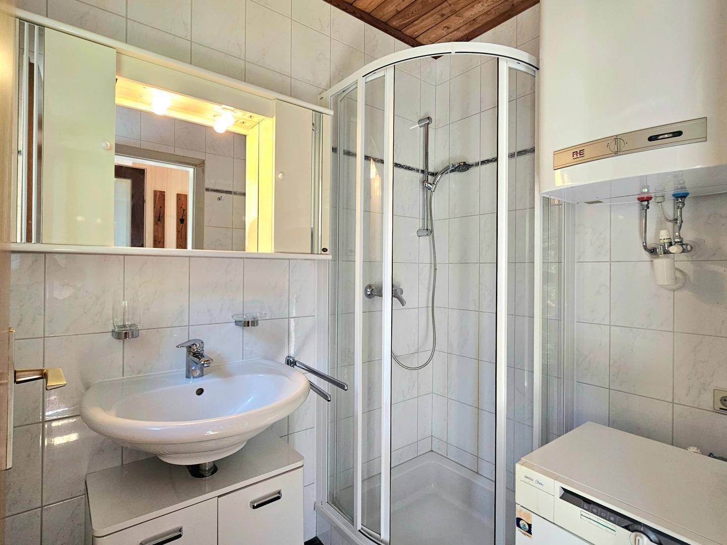 Helles Badezimmer mit Eckdusche, Waschbecken und praktischem Spiegelschrank unter Holzbalkendecke.