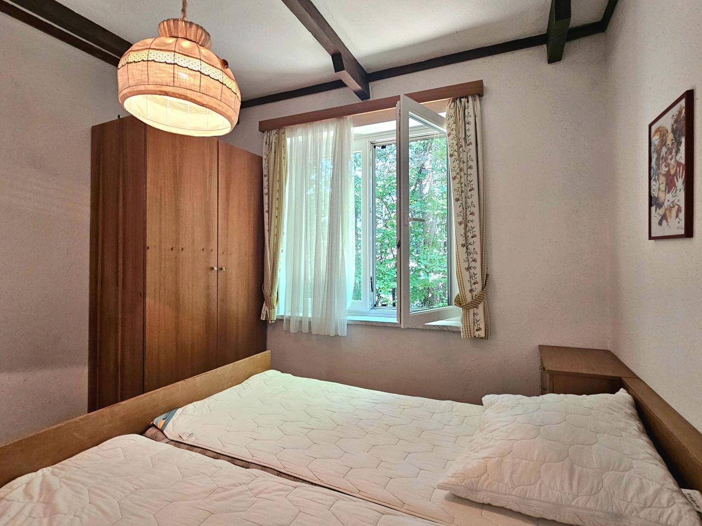 Schlafzimmer mit großem Holzschrank, zwei Einzelbetten und Fenster mit Blick auf die Natur.