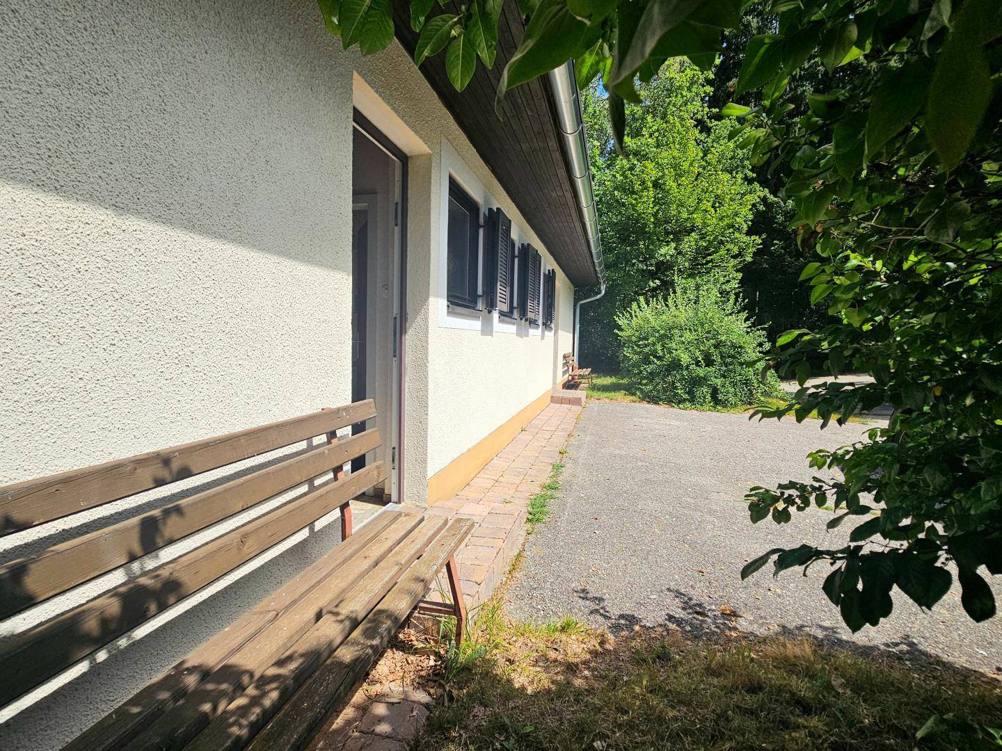 Detailansicht der Hauswand mit einer Holzbank und Blick auf den Kiesweg.