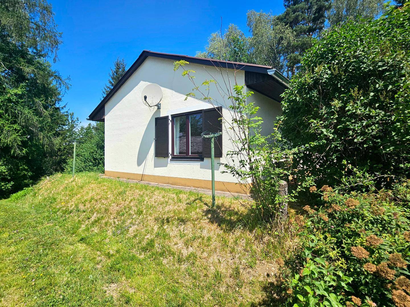 Seitenansicht eines kleinen Hauses mit Satellitenschüssel und grüner Umgebung.