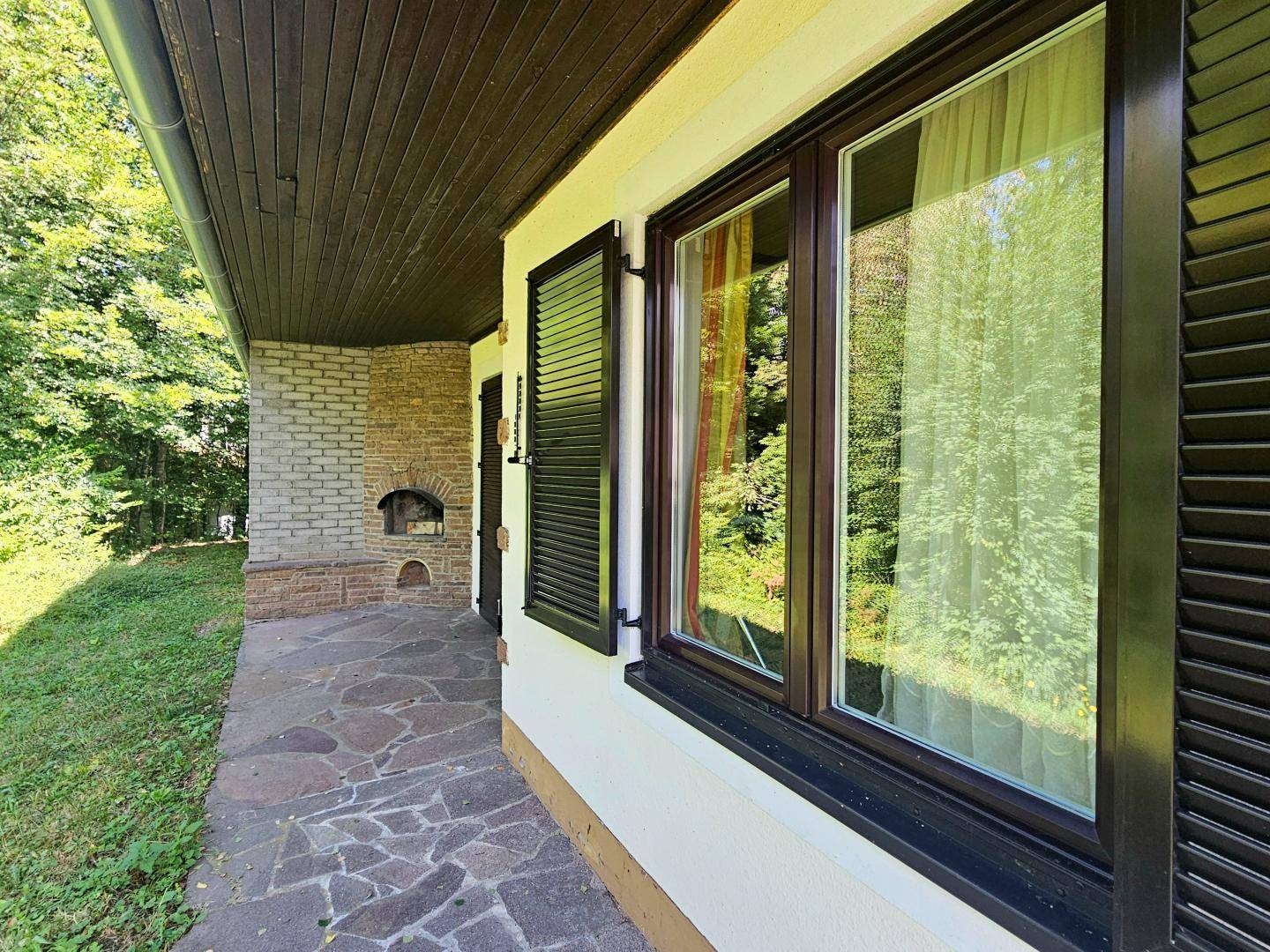 Detailansicht der Terrasse mit Steinboden, Außenkamin und Fenster mit Fensterläden.