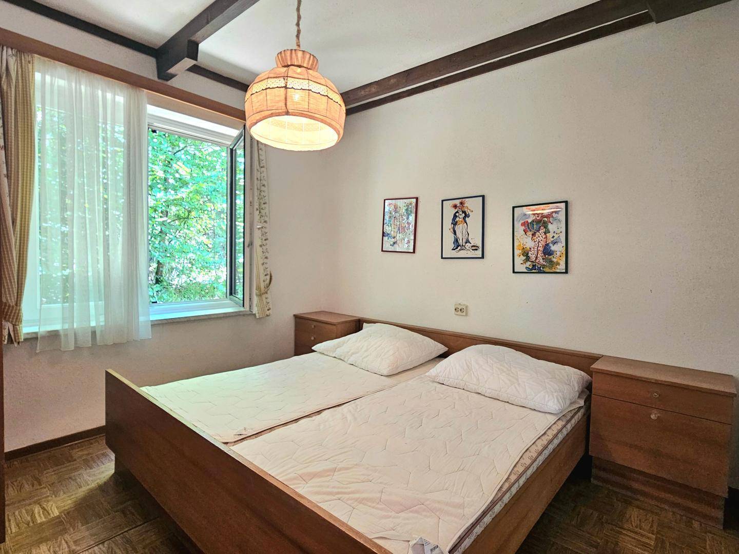 Schlafzimmer mit zwei Einzelbetten, Nachttischen und Blick ins Grüne durch das Fenster.