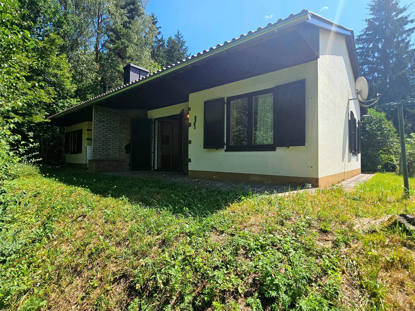 Vorderansicht des Hauses mit einer kleinen Terrasse und umgebender Natur.