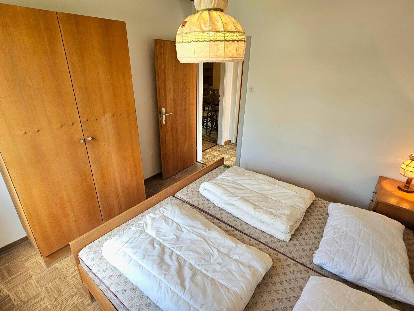Schlafzimmer mit Holzschrank und Blick in den Flur, ausgestattet mit zwei Einzelbetten.