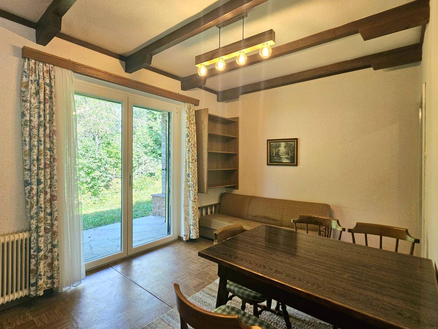 Wohn- und Essbereich mit Holztisch, Sofa und Zugang zur Terrasse mit Blick ins Grüne.