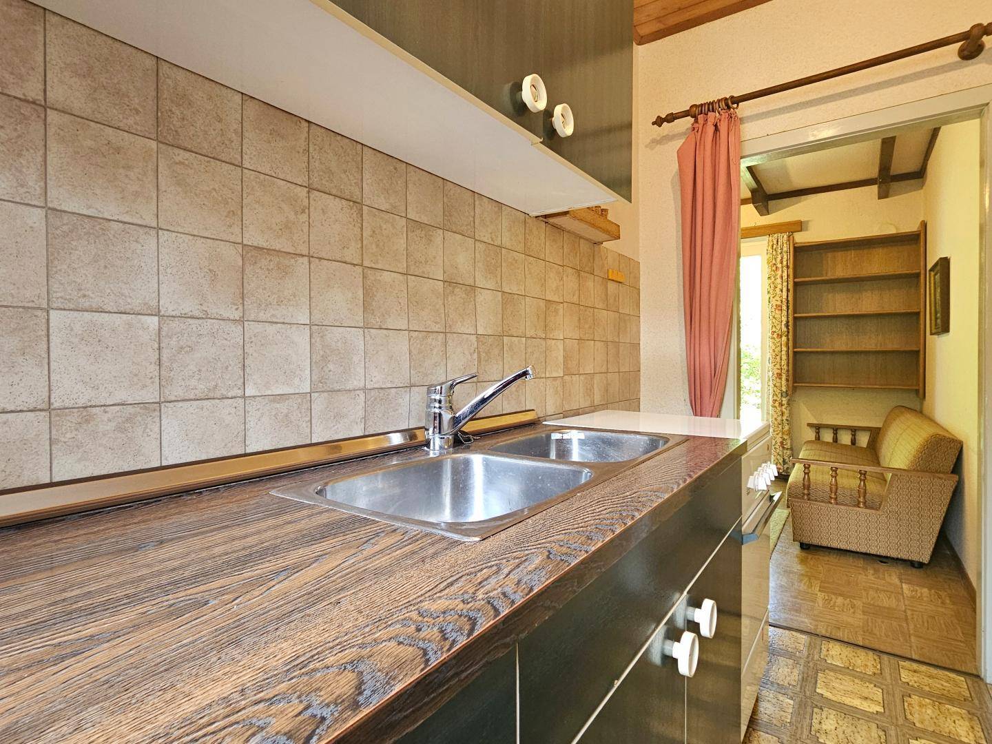 Einfache Küche mit Holz-Arbeitsplatte, Doppelspüle und Blick in den Wohnbereich.