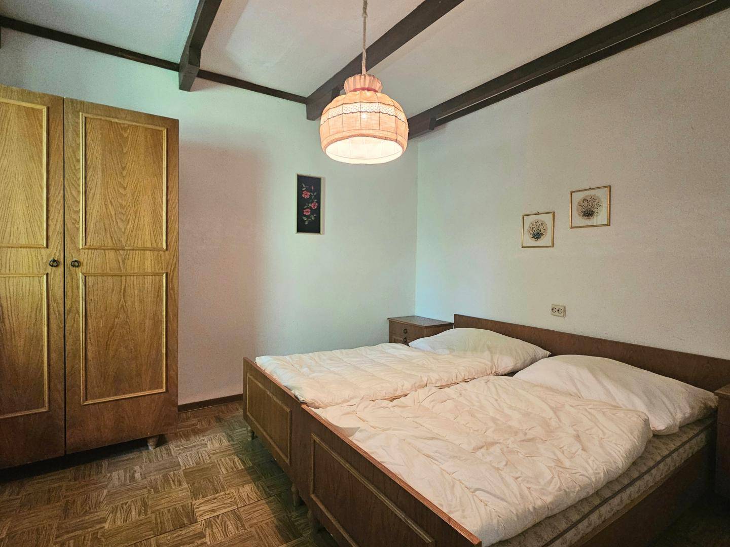 Schlafzimmer mit traditionellem Holzschrank und zwei Einzelbetten unter Holzbalkendecke.