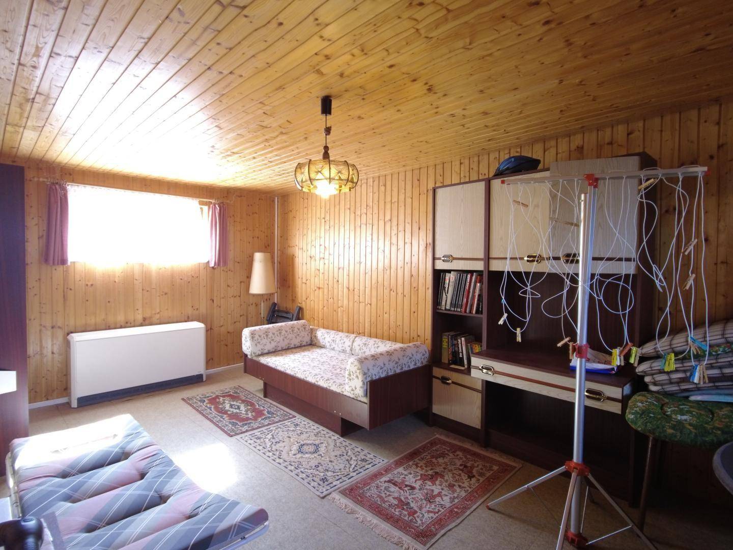 Vielseitiger Raum mit Holzvertäfelung, Fenster, Tagesbett, Schrankwand und einem Wäscheständer.