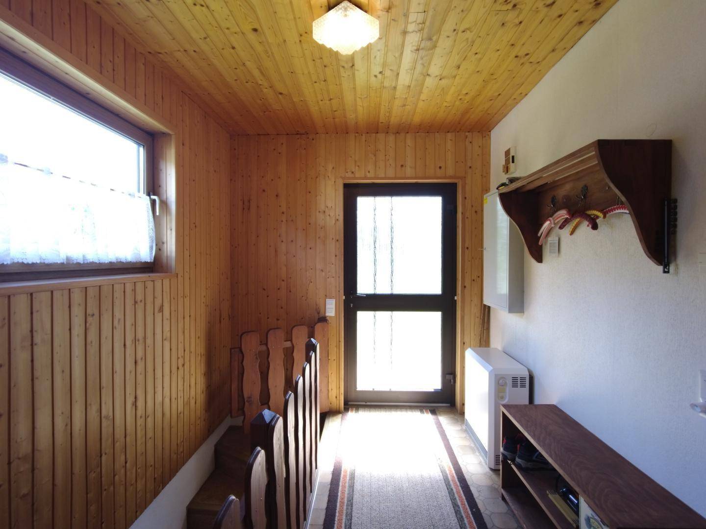 Heller Flur mit Holzvertäfelung, Treppe und Eingangstür mit viel Tageslicht.