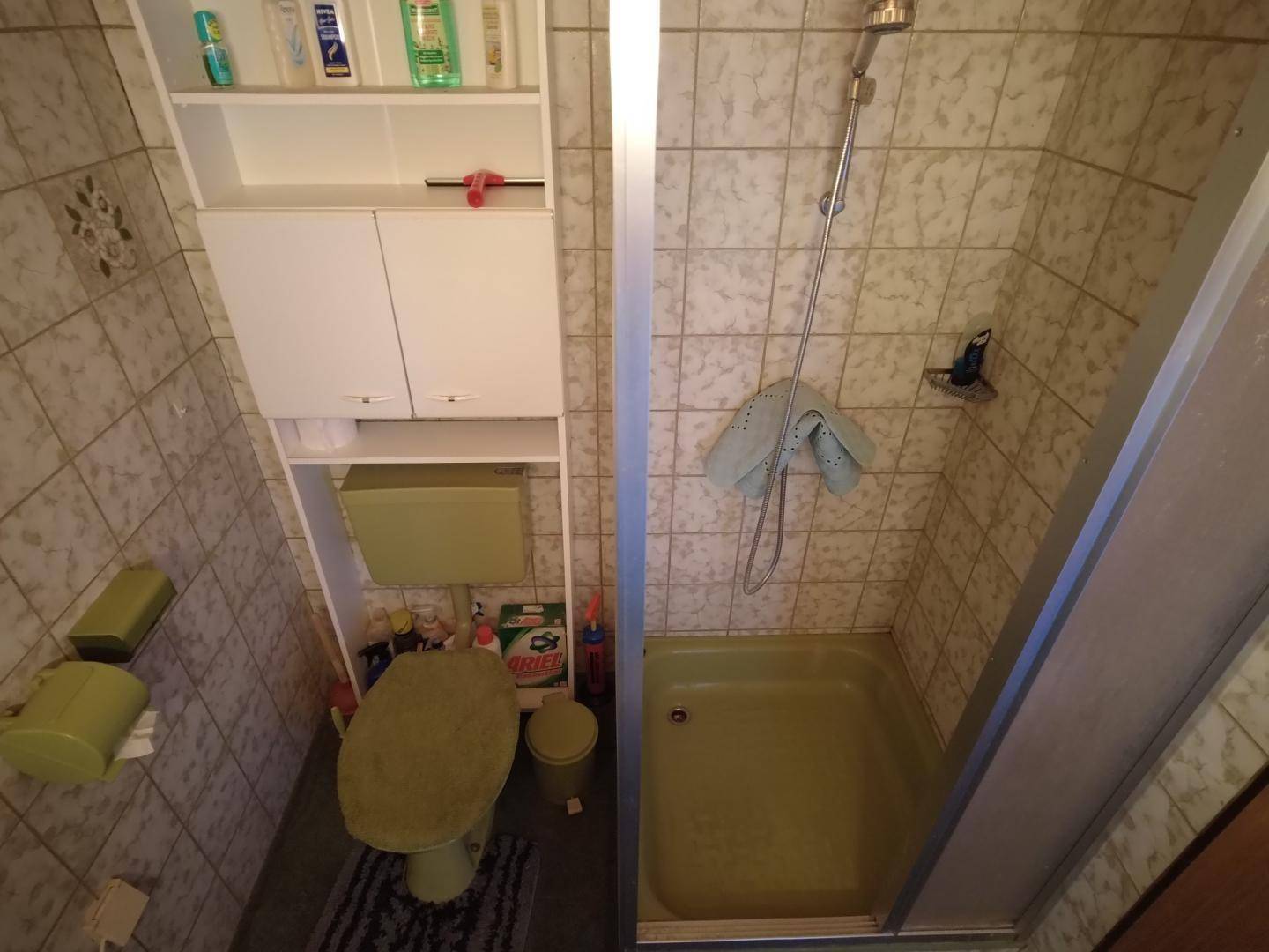 Kleines Badezimmer mit grüner Toilette, Duschkabine und Wandfliesen, ergänzt durch einen praktischen Hochschrank.