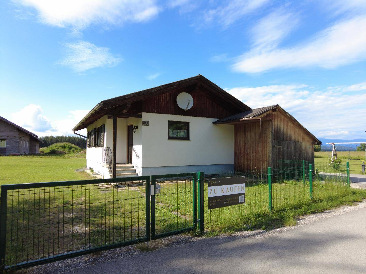Freistehendes Haus mit "Zu Kaufen" Schild am Gartenzaun und weitem Blick.