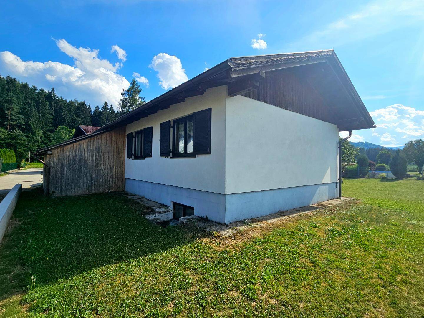 Seitliche Ansicht des Hauses mit weißer Fassade, Holzverkleidung und grüner Rasenfläche.