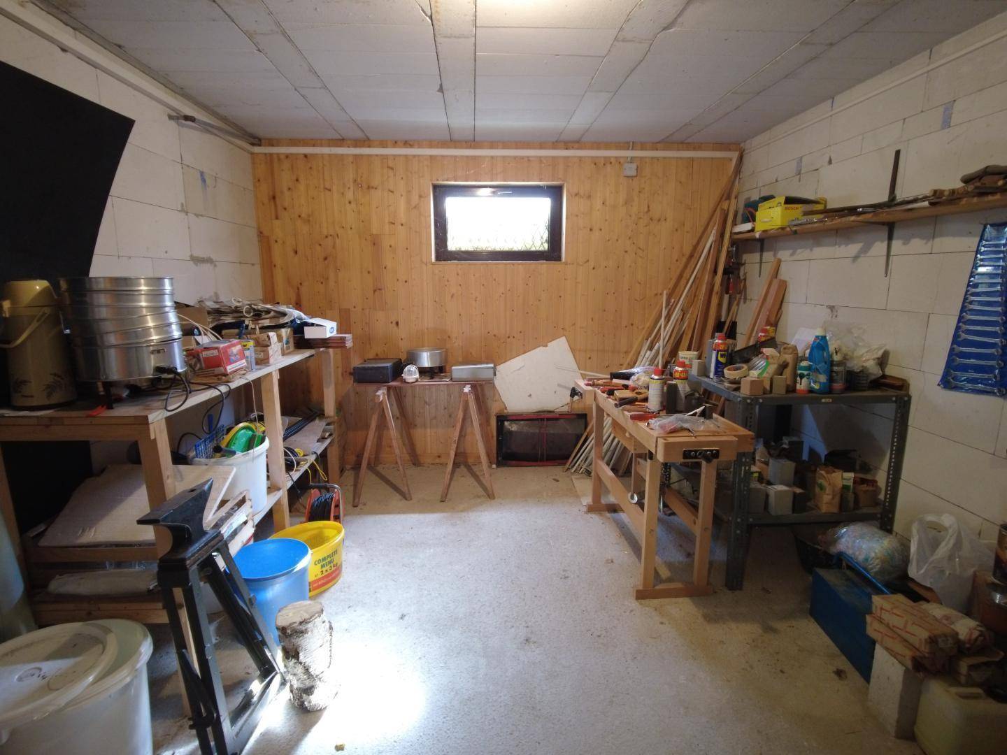 Werkstatt im Keller mit Betonsteinwänden, Holzvertäfelung, kleinem Fenster und verschiedenen Werkbänken und Regalen.