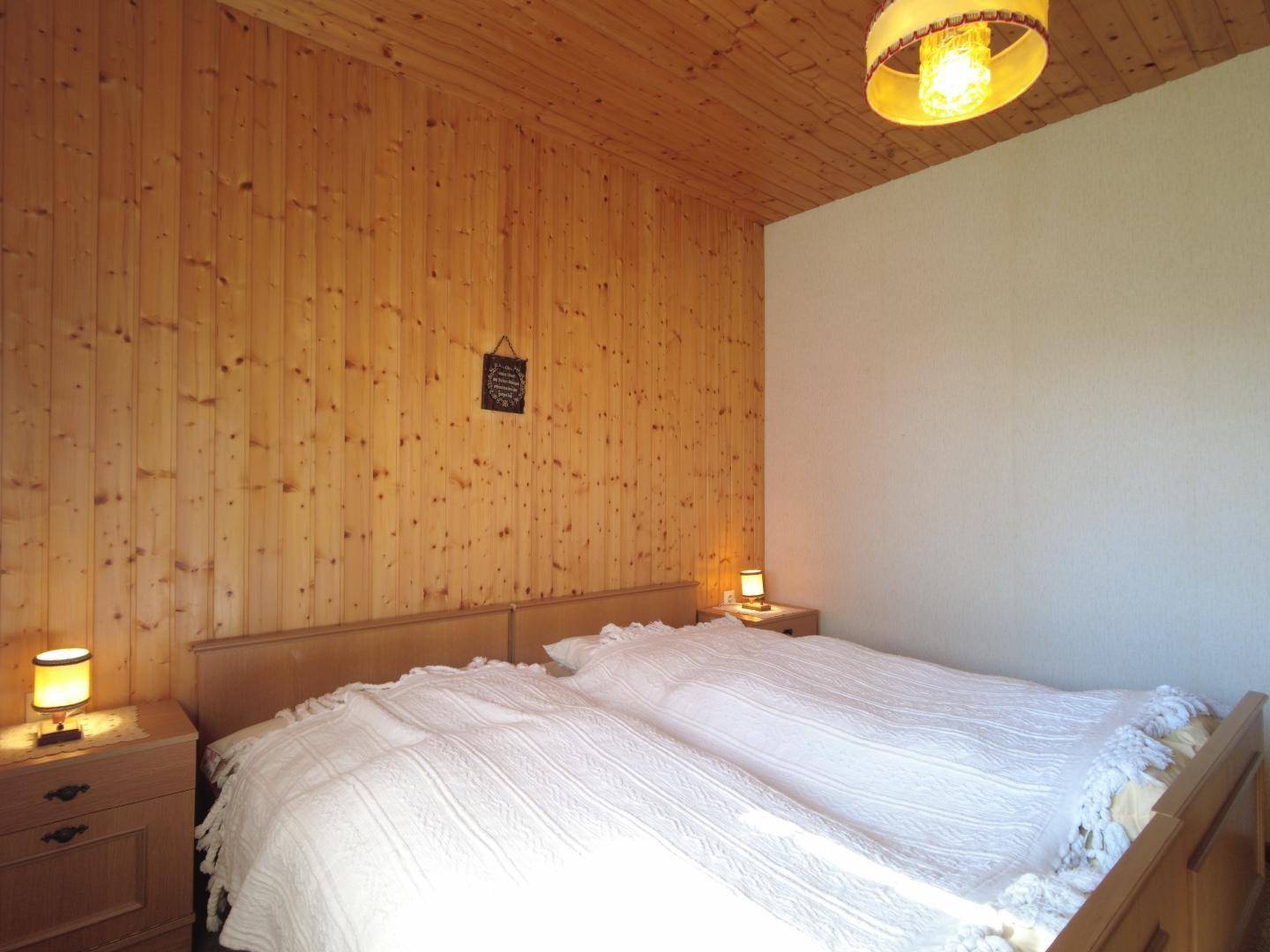 Gemütliches Schlafzimmer mit Holzvertäfelung an Wänden und Decke, ausgestattet mit zwei Einzelbetten und Nachttischen.