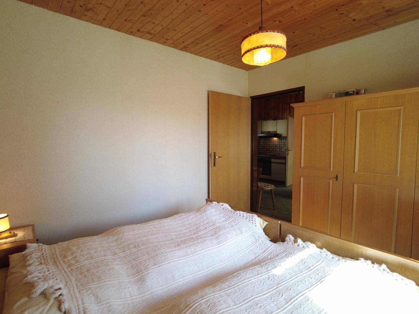Schlafzimmer mit Holzvertäfelung, Kleiderschrank und Zugang zu einem angrenzenden Küchenbereich.