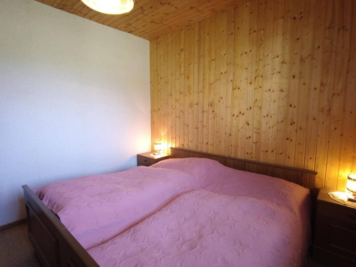 Gemütliches Schlafzimmer mit Holzvertäfelung, rosa Bettwäsche und Nachttischen, die eine warme Atmosphäre schaffen.