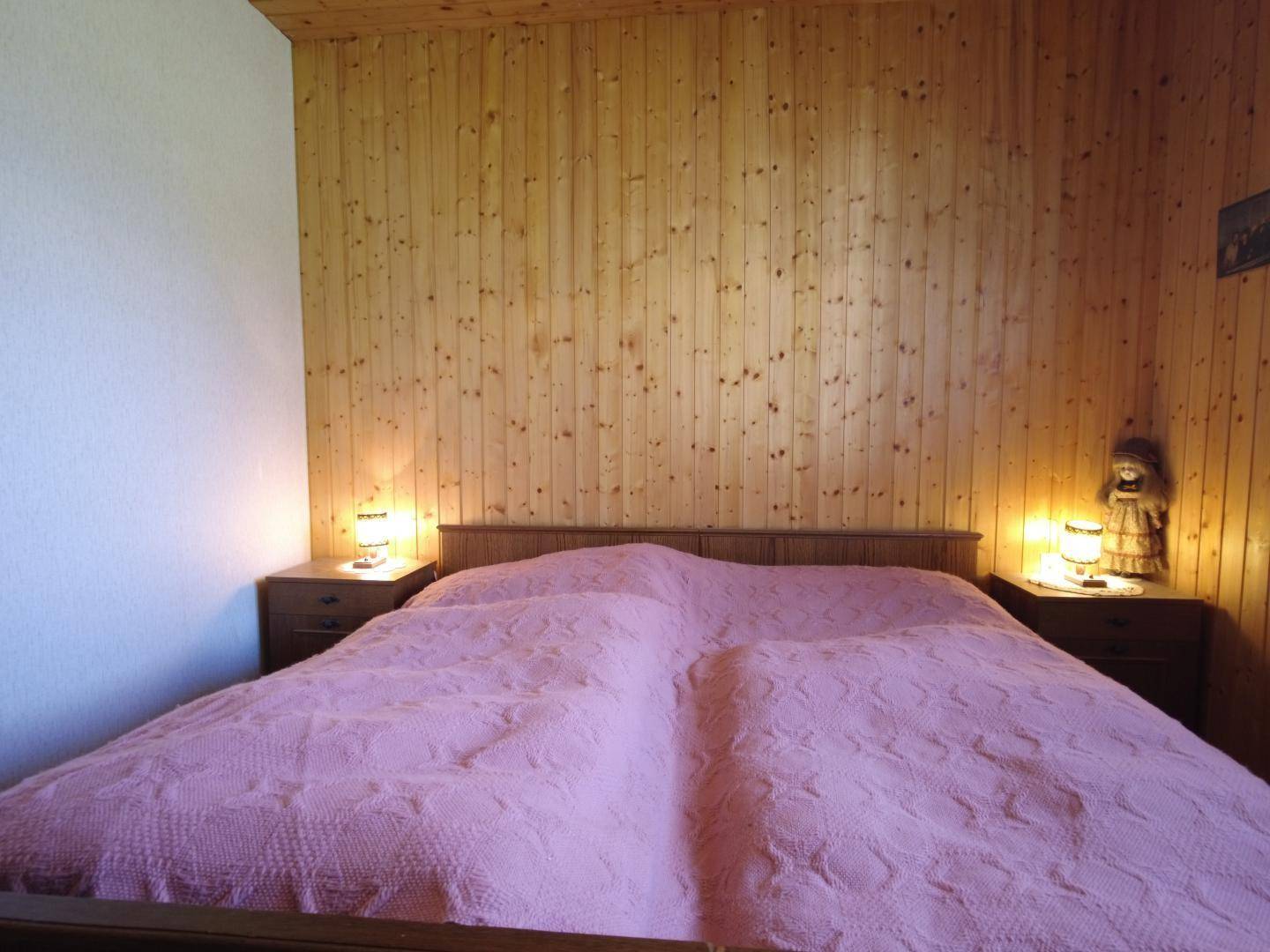 Schlafzimmer mit Holzvertäfelung und zwei Betten, die mit rosa Tagesdecken für eine gemütliche Atmosphäre versehen sind.