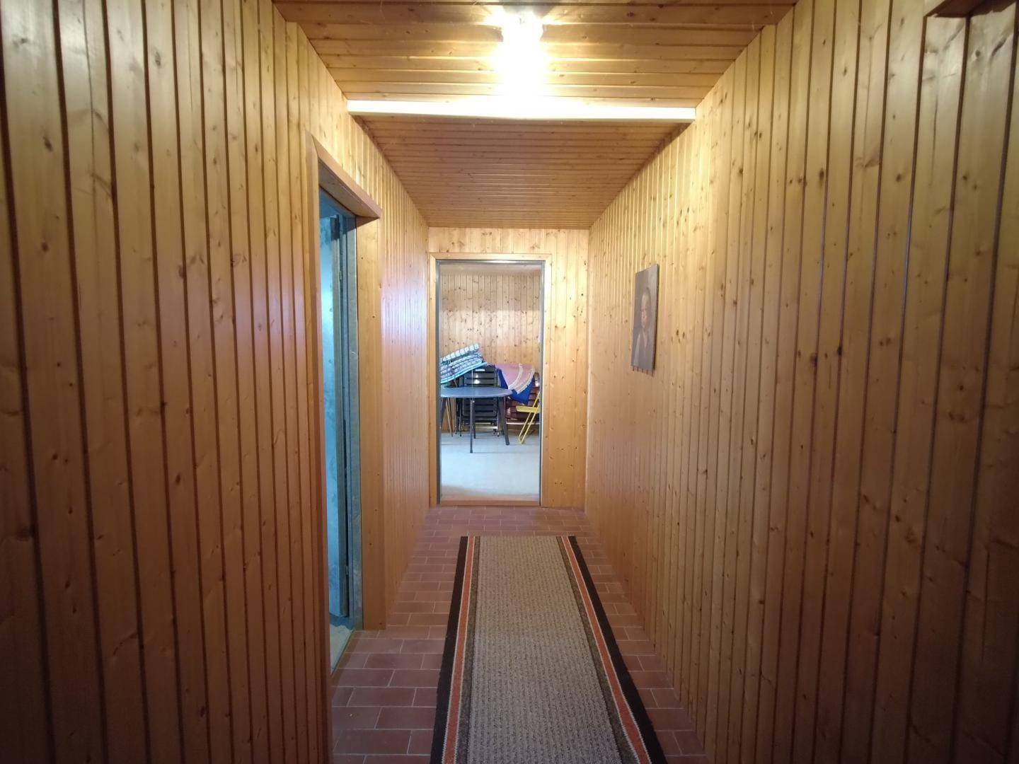 Langer Flur mit Holzvertäfelung an Wänden und Decke, Ziegelboden und einem Teppichläufer, der zu einem weiteren Raum führt.