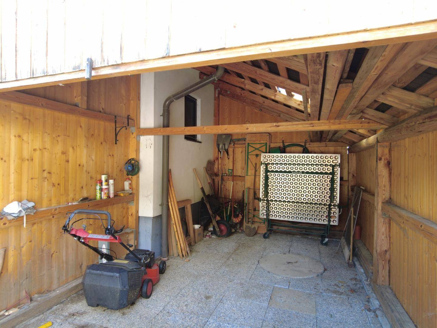 Innenansicht der Holzgarage mit Werkzeugen, Rasenmäher und offenem Dachstuhl.