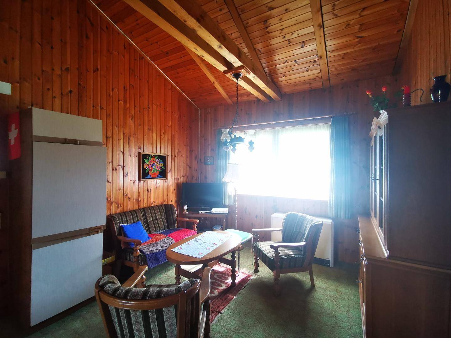 Gemütliches Wohnzimmer mit Holzvertäfelung, traditionellen Möbeln und hellem Fenster.