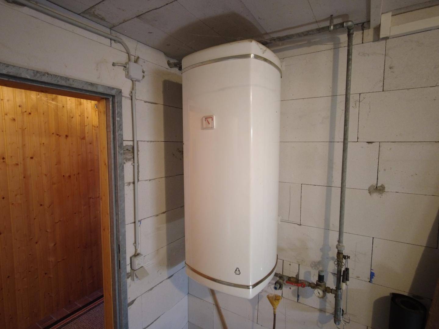 Nahaufnahme eines Warmwasserbereiters an einer Betonsteinwand in einem Hauswirtschaftsraum.