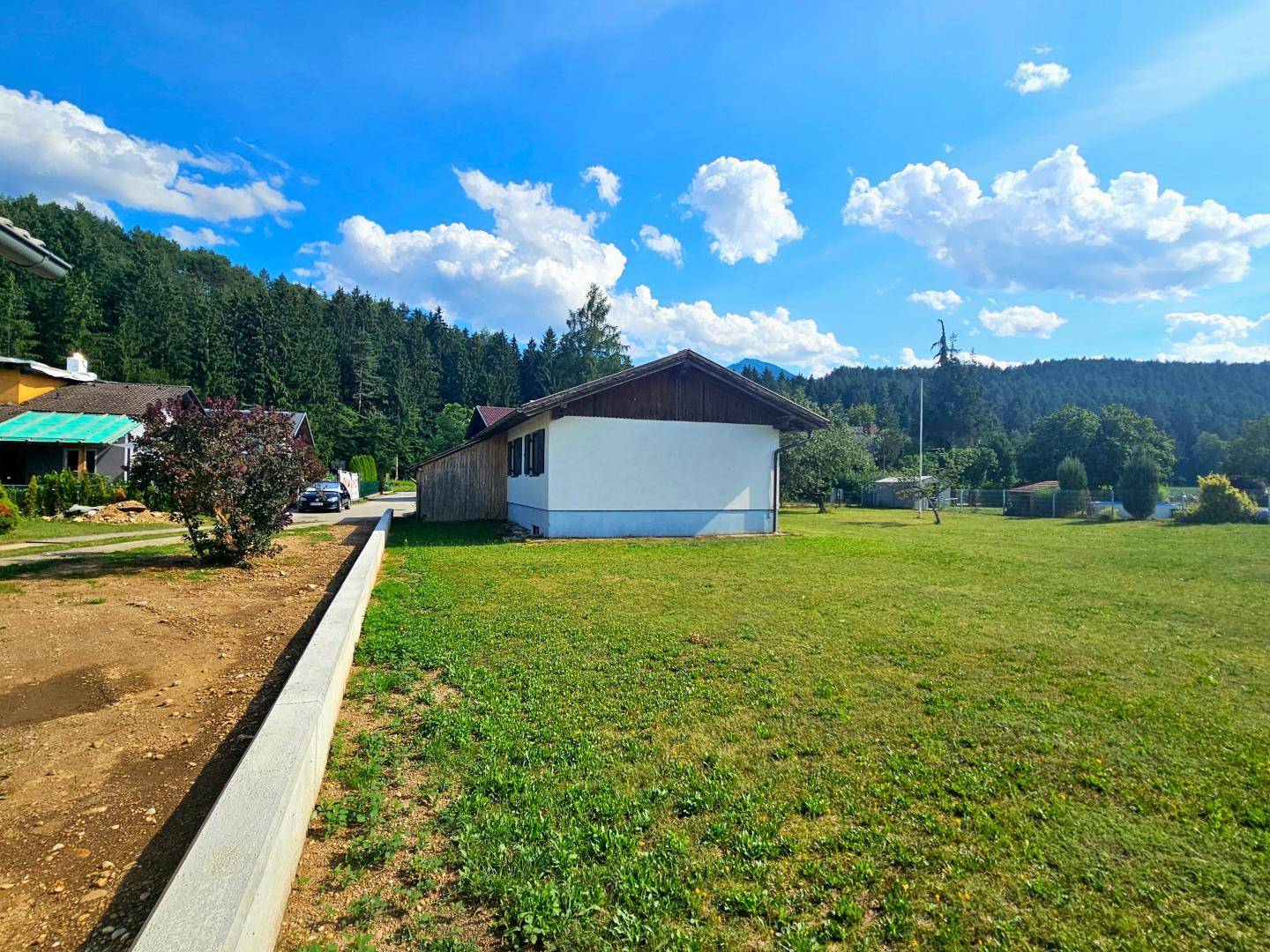 Weitläufige Rasenfläche des Gartens mit dem Haus im Hintergrund und bewaldeten Hügeln.