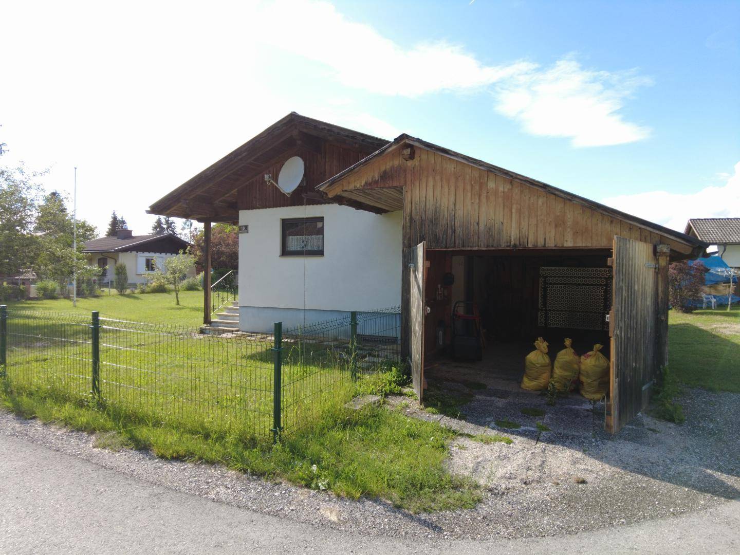 Einfamilienhaus mit angrenzender offener Garage oder Schuppen und umzäuntem Gartenbereich.