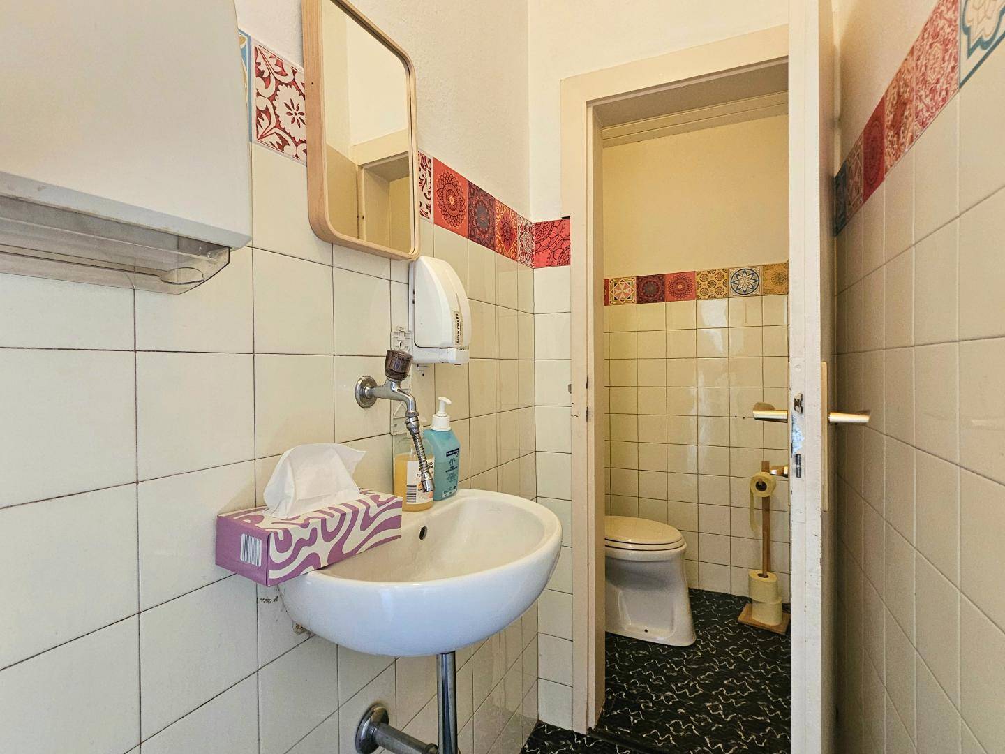 Kleine Toilette mit Waschbecken, Spiegel und Fliesen an Wänden und Boden.