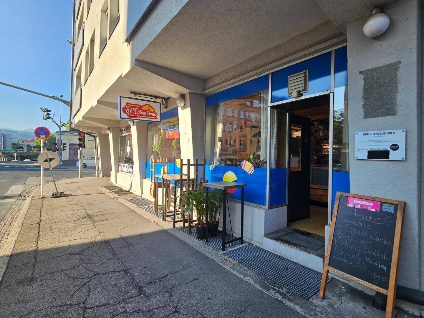 Weitläufige Außenansicht des Restaurants mit blauer Fassade, Außentischen und der umliegenden Straße.