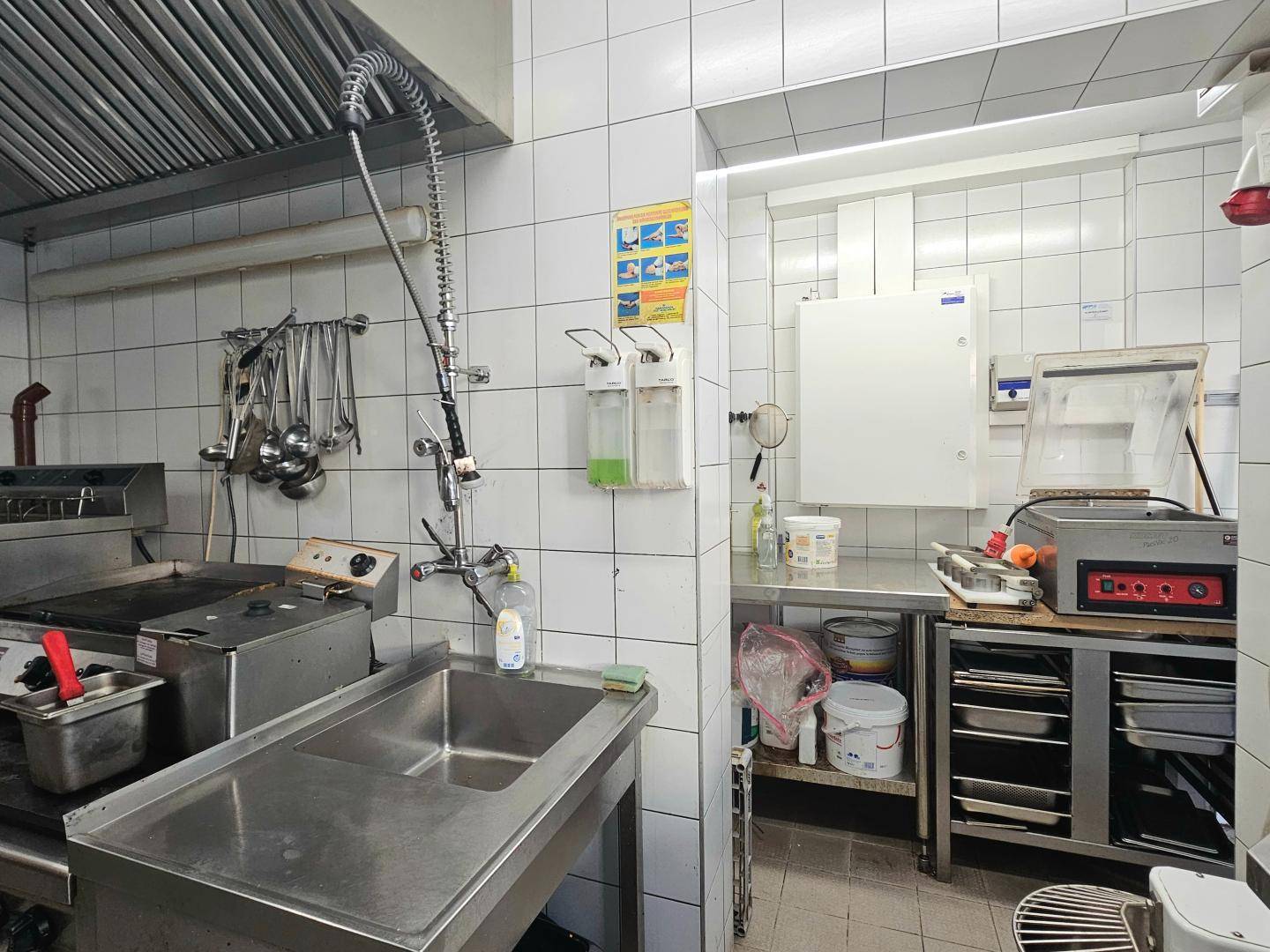 Teilansicht einer Großküche mit großem Doppelwaschbecken aus Edelstahl und Zugang zu einem Nebenraum.