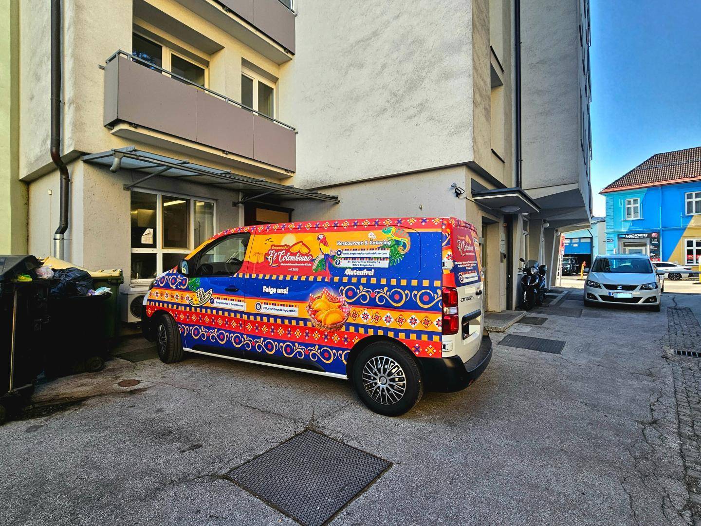 Außenansicht eines Gebäudes mit einem auffällig bemalten Lieferwagen vor dem Eingangsbereich.