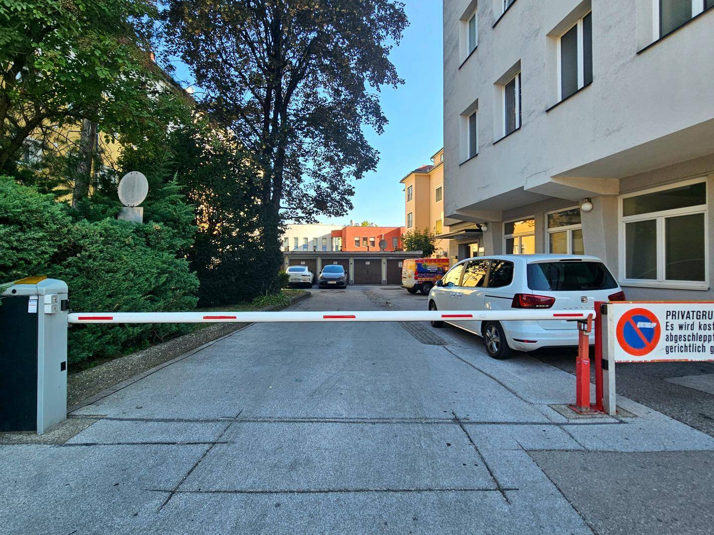 Private Zufahrt mit Schranke und Hinweisschild, die zu Parkplätzen oder Garagen hinter dem Gebäude führt.