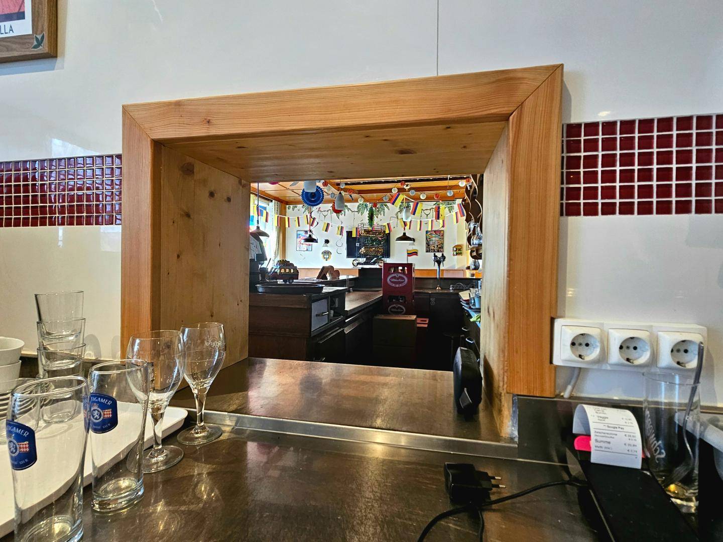 Blick von der Theke in einen festlich dekorierten Gastraum mit Holzdurchreiche und Edelstahlflächen.