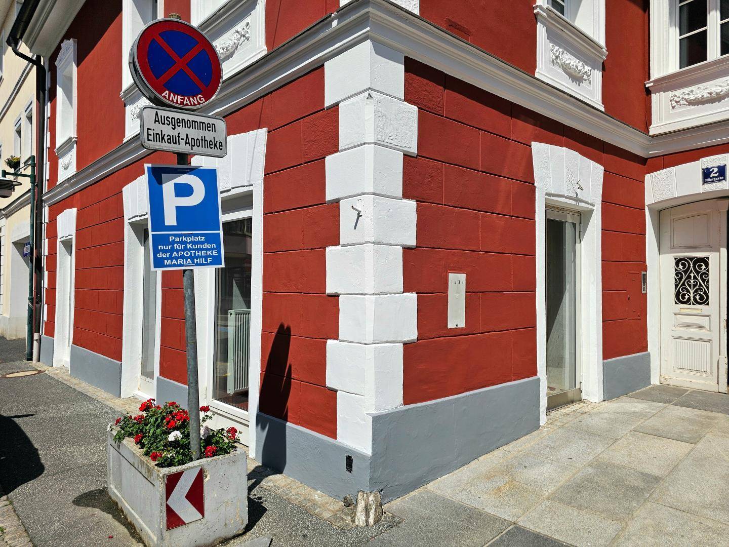 Gebäudeecke mit roter Fassade, weißen Ecksteinen und einem Parkplatzschild für Kunden der Apotheke.