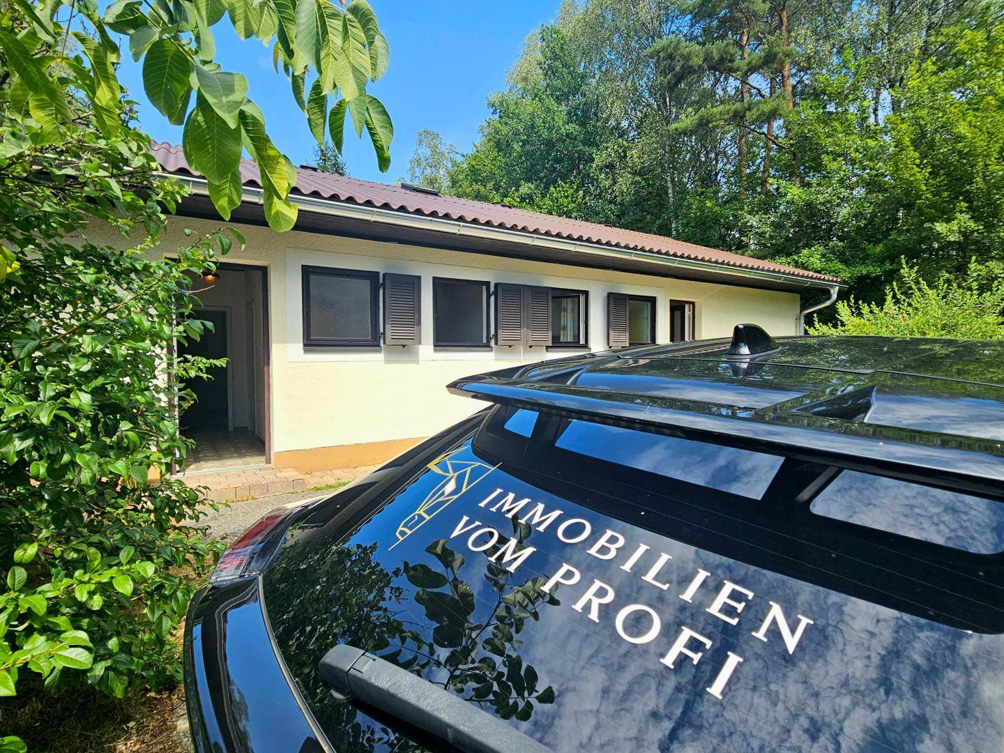 Nahaufnahme der Gebäudefassade mit Fenstern und Fensterläden, umgeben von Bäumen und Sträuchern.