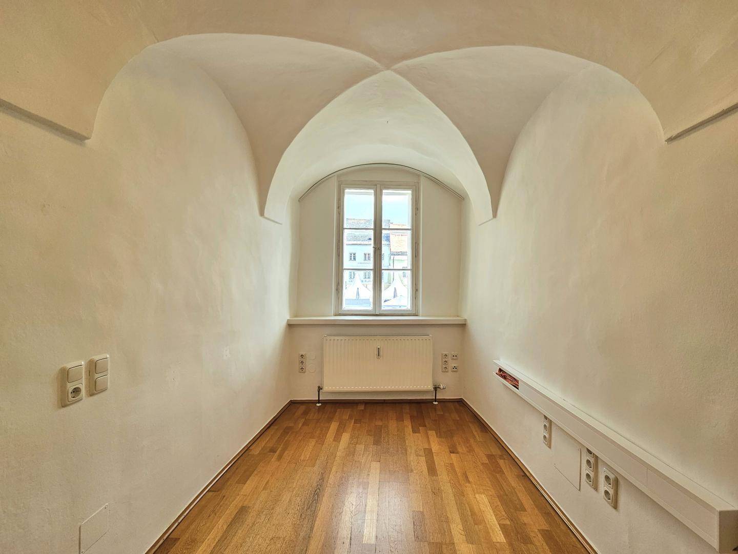 Kleiner Raum mit Gewölbedecke, Fenster und Holzboden, ideal für individuelle Nutzung.