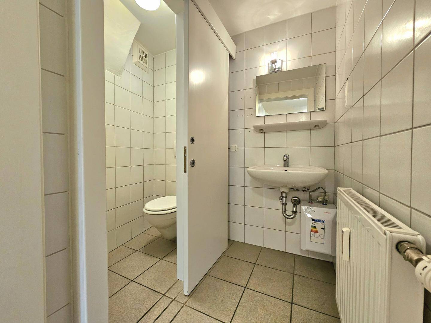 Modernes WC mit Fliesen, Waschbecken, Spiegel und Heizkörper.