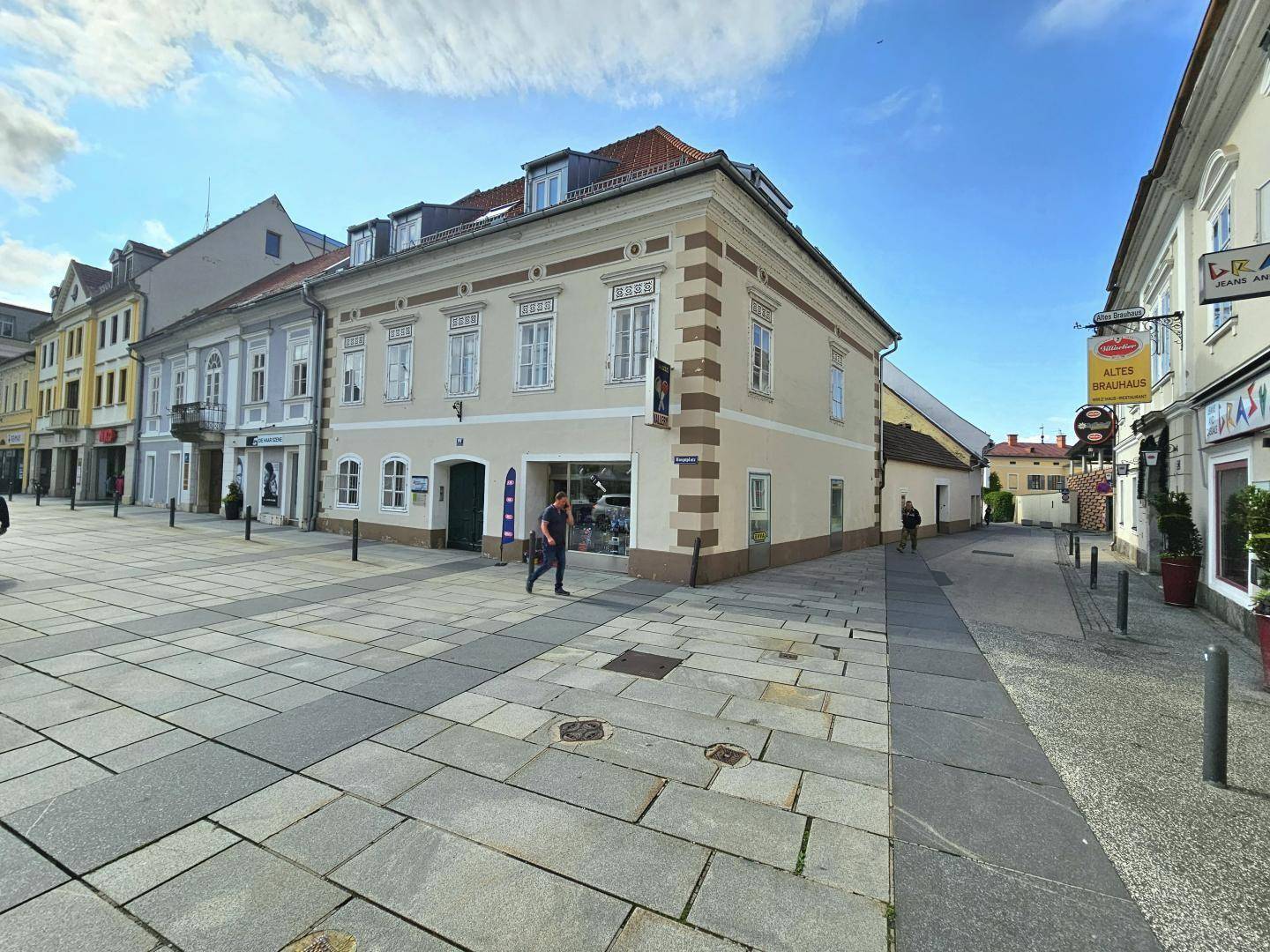 Historisches Gebäude an einem belebten Stadtplatz mit Geschäften und Fußgängern.