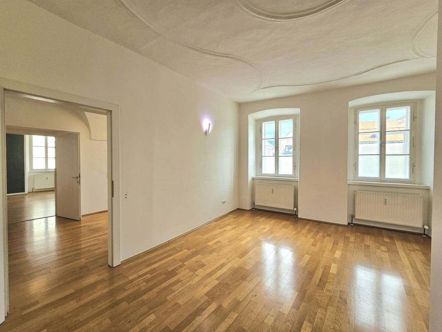 Geräumiges Zimmer mit Parkettboden und zwei Fenstern, die viel Licht spenden.