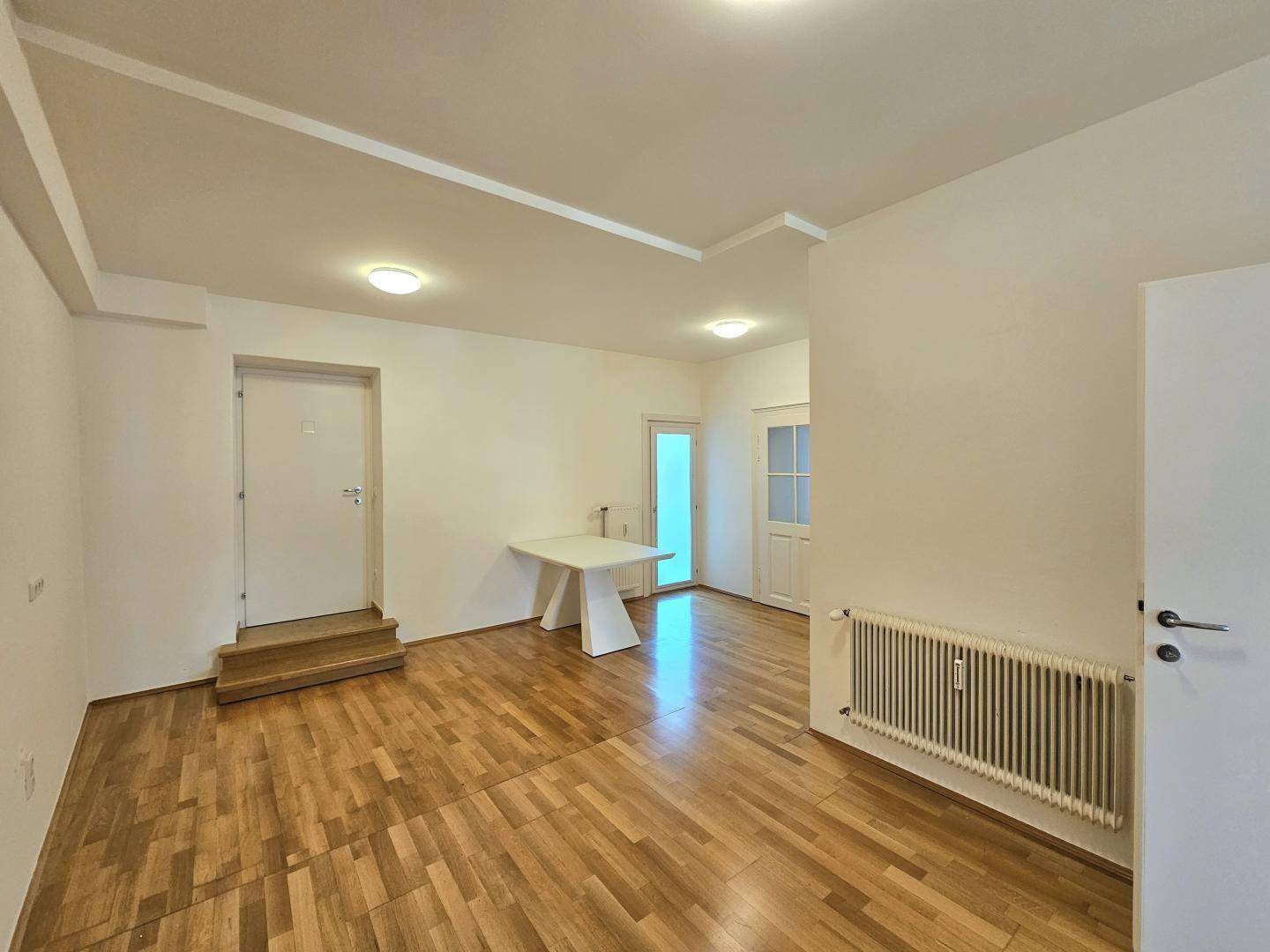 Geräumiger Raum mit Holzboden und einem modernen Tisch, ideal als Ess- oder Wohnbereich.