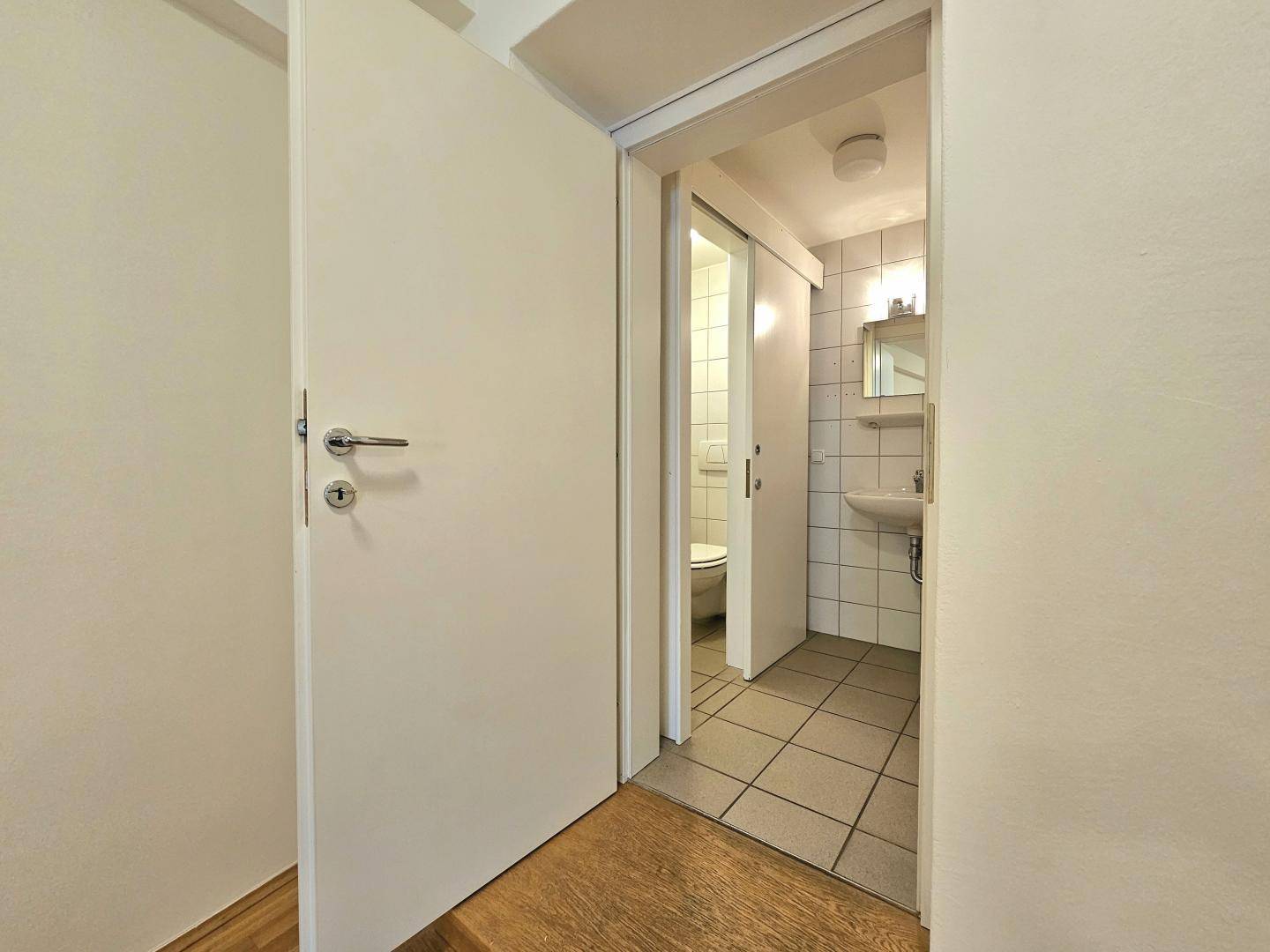 Kleines WC mit Fliesenboden, Waschbecken und Schiebetür.
