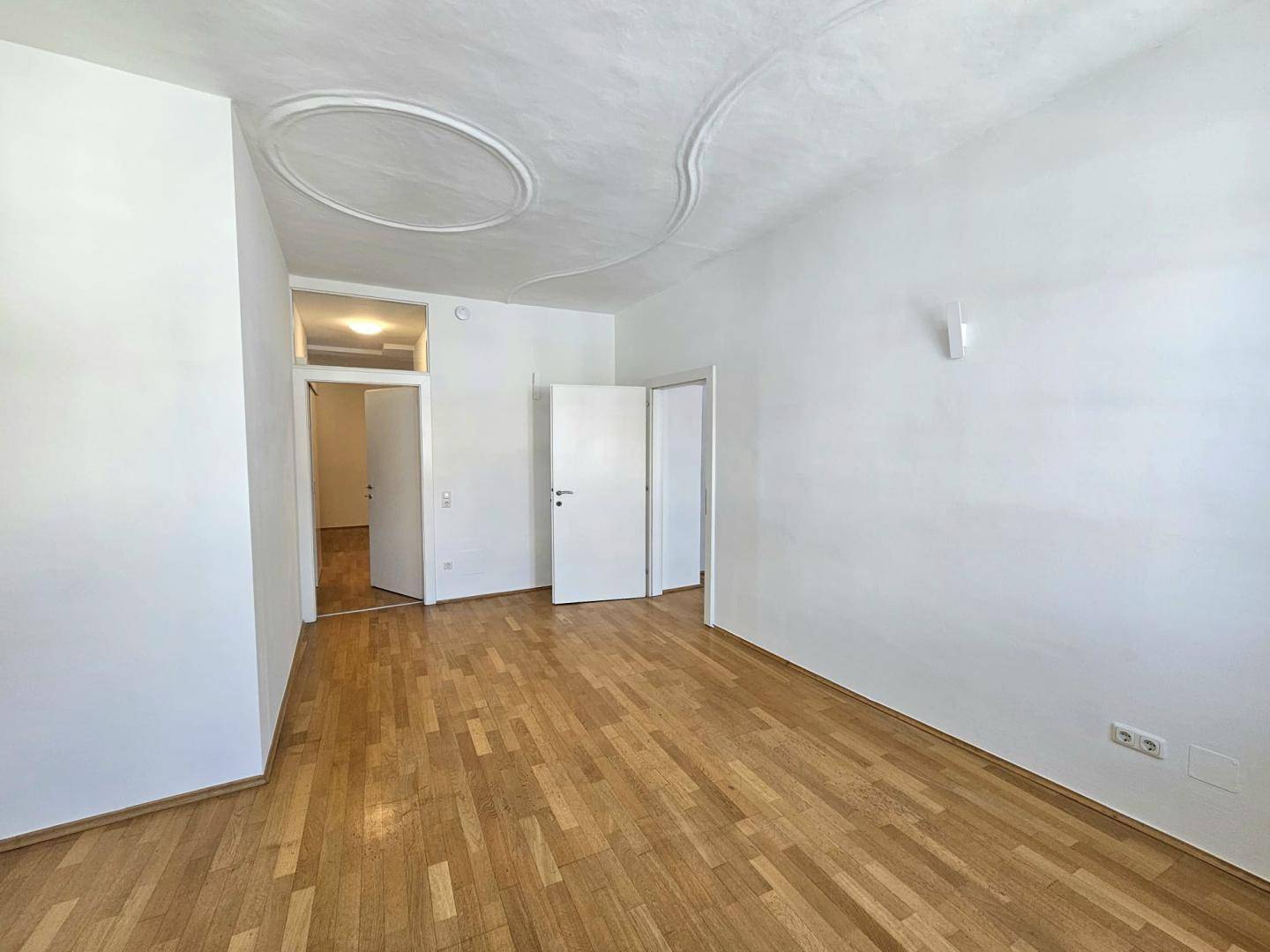 Geräumiges Zimmer mit Parkettboden und dekorativer Stuckdecke, bereit zur Nutzung.