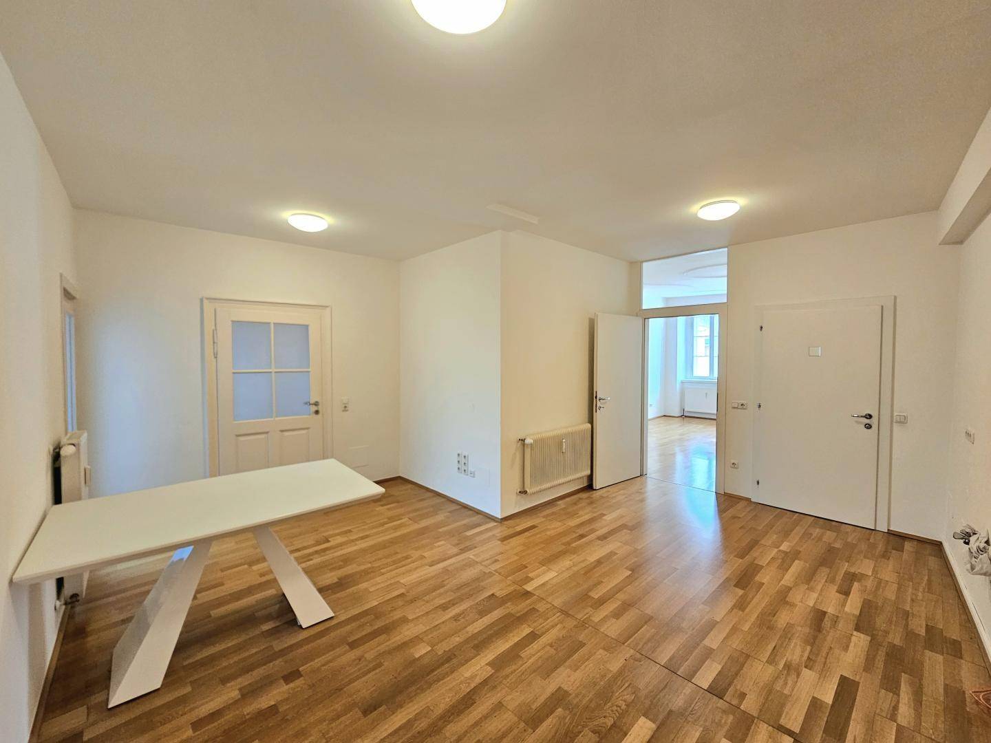 Großer Raum mit Holzboden und modernem Tisch, ideal für Wohn- oder Essbereich.