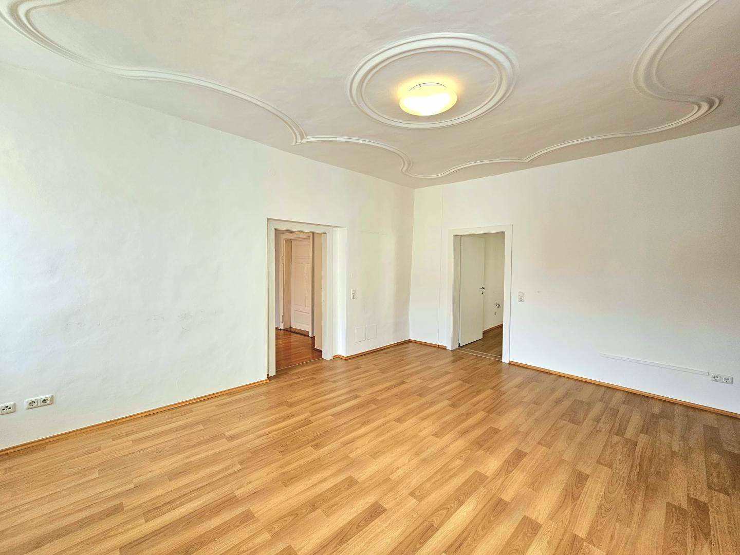 Geräumiges Zimmer mit Parkettboden und dekorativer Stuckdecke, bereit zur Nutzung.