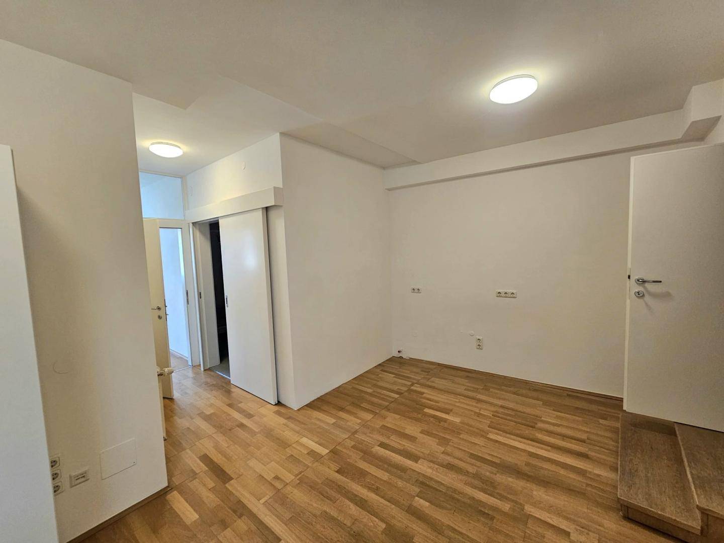 Heller Raum mit Holzparkettboden und Schiebetüren, der als Übergangsbereich dient.