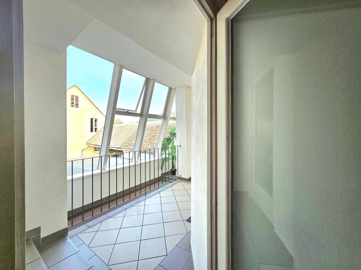 Heller, verglaster Balkon mit Fliesenboden und Blick auf die umliegenden Dächer und Gebäude.