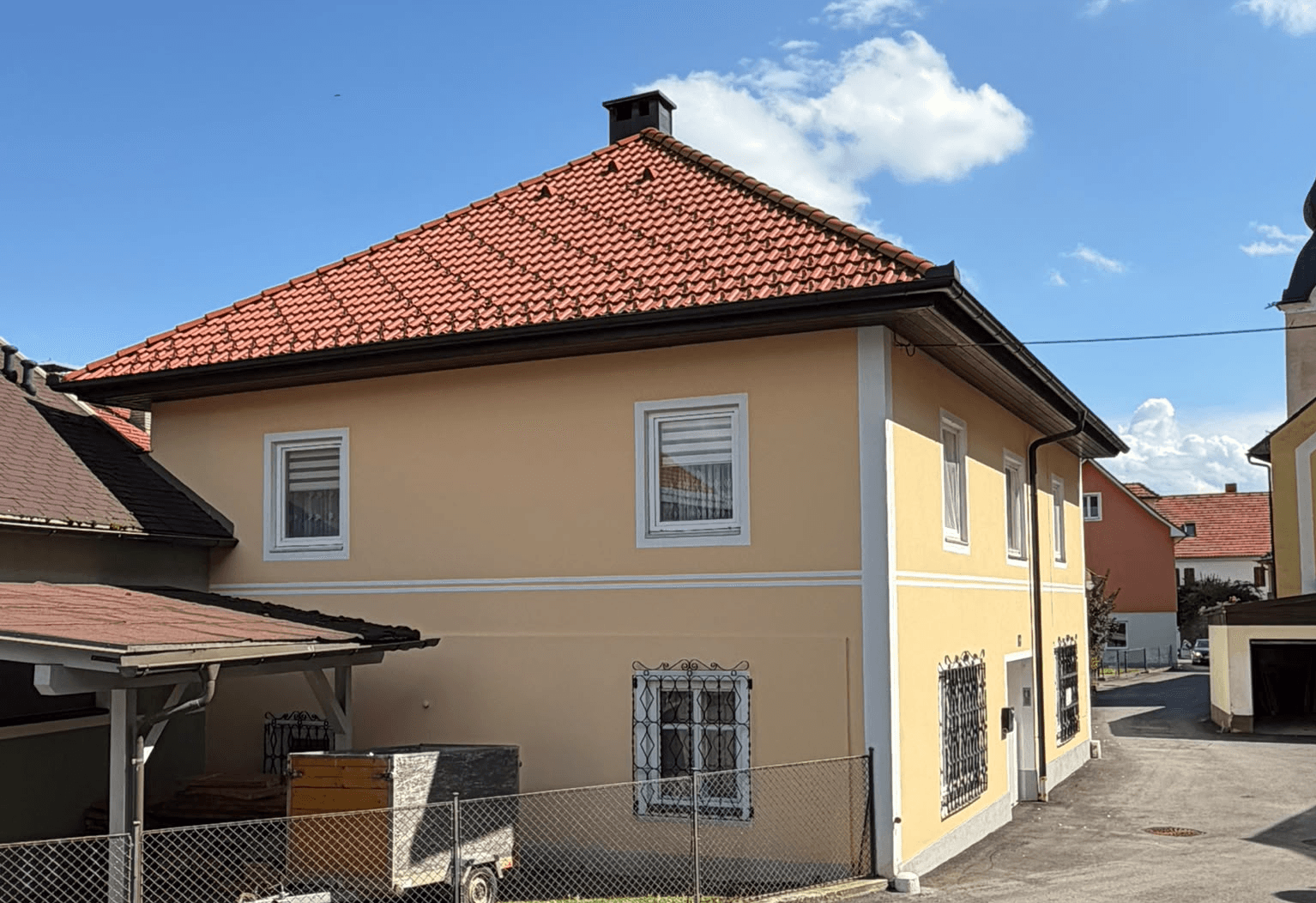 Seitenansicht des gelben Wohnhauses mit rotem Ziegeldach und Blick auf die Umgebung.