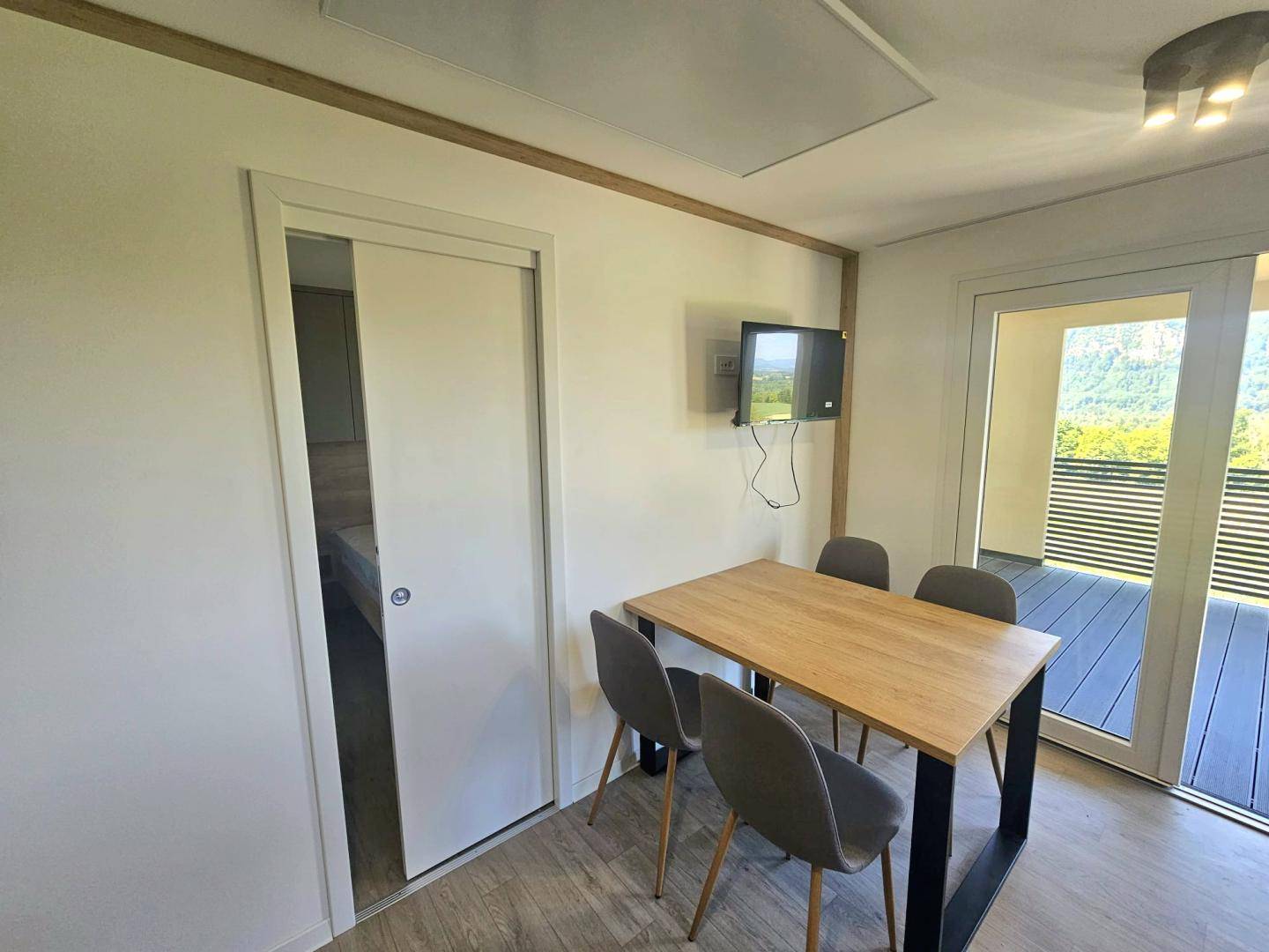 Essbereich mit Holztisch und Stühlen, angrenzend an den Wohnbereich mit Zugang zur Loggia.